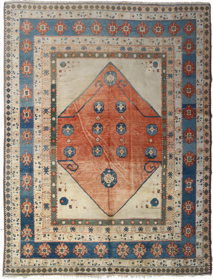 A Turkish wool rug with a red and blue geometric pattern and a visible moth damage.