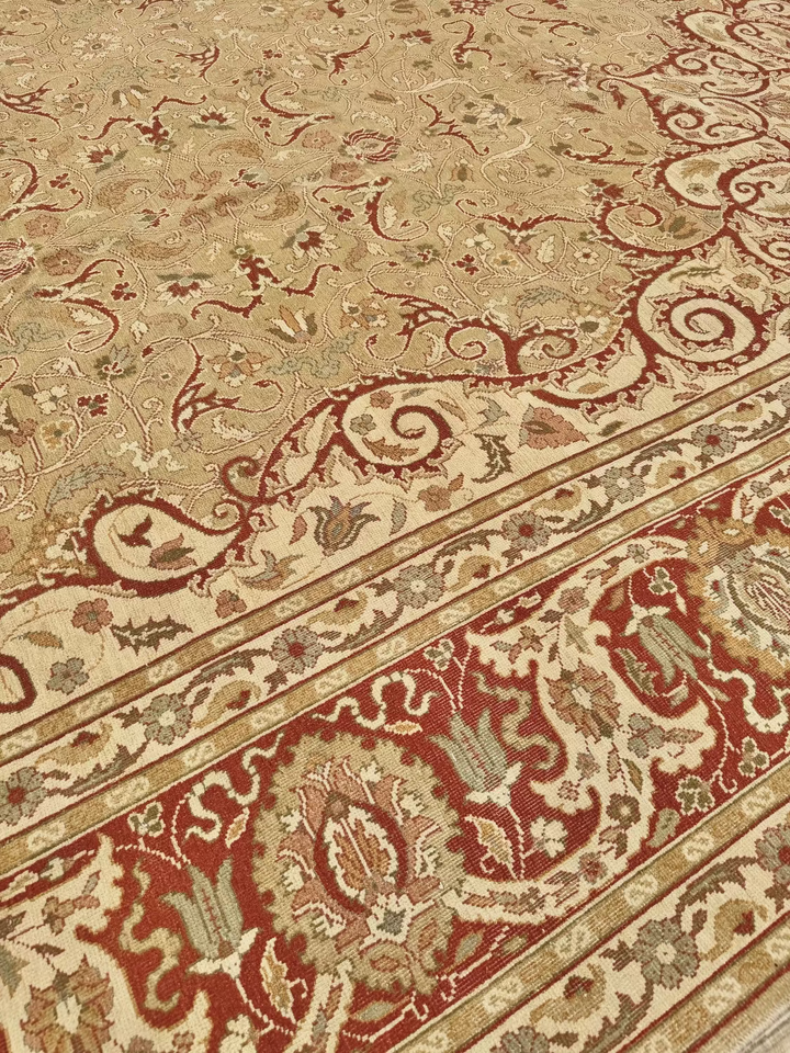 A close-up of an ornate area rug with a beige field, deep red borders, and intricate floral and scroll motifs in cream, rust, and muted green.