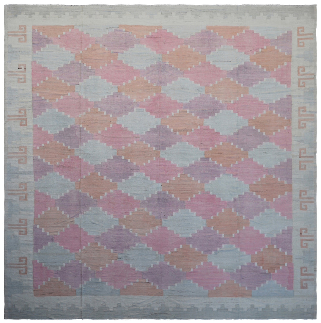 A flat-weave kilim-style area rug with a geometric plaid pattern in pink and purple shades, featuring intricate border designs.