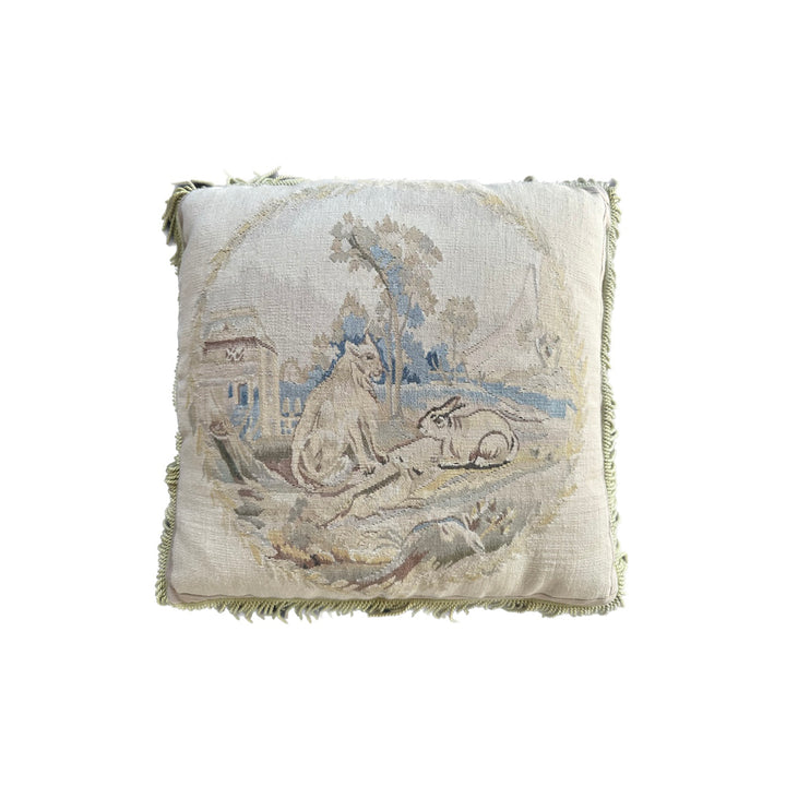 Handcrafted 24x24 beige and blue wool Aubusson style cushion featuring a whimsical animal motif and vibrant green fringe tassels by Ariana Rugs
