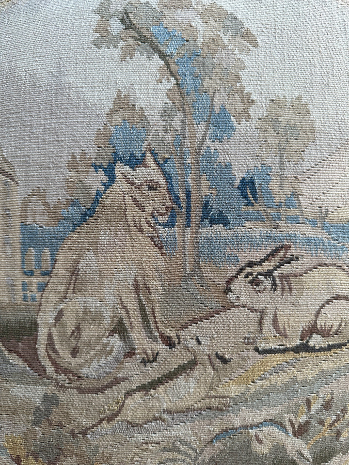 Handcrafted 24x24 beige and blue wool Aubusson style cushion featuring a whimsical animal motif and vibrant green fringe tassels by Ariana Rugs