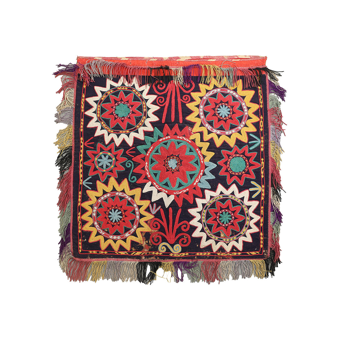 Colorful embroidered textile with geometric patterns and fringes on a white background