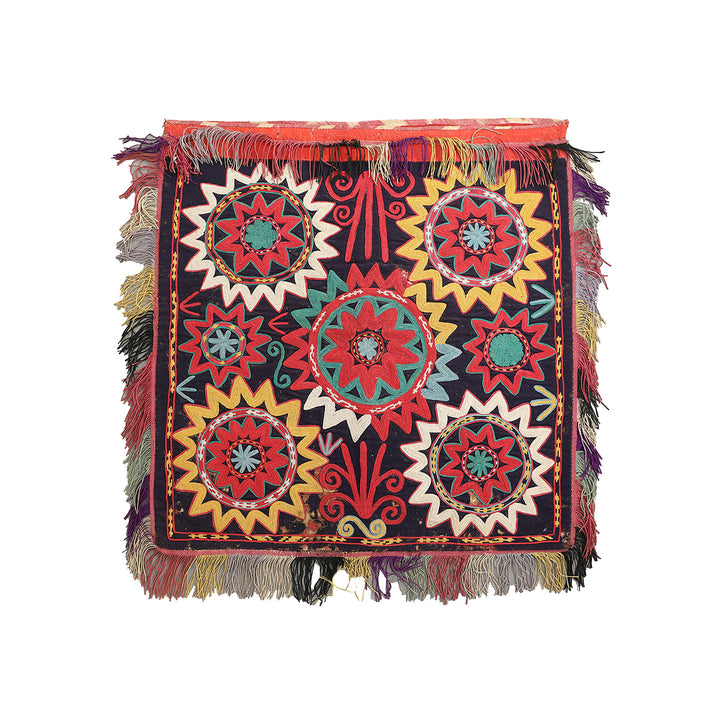 Colorful embroidered textile with geometric patterns and fringes on a white background