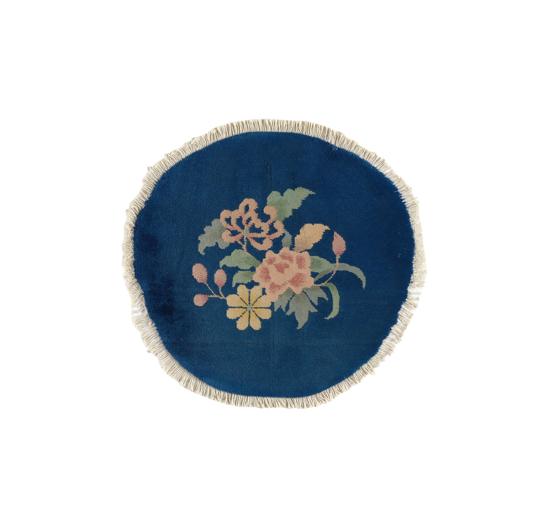 A small, round, blue vintage area rug with a central floral design and a fringed edge.