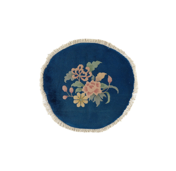 A small, round, blue vintage area rug with a central floral design and a fringed edge.