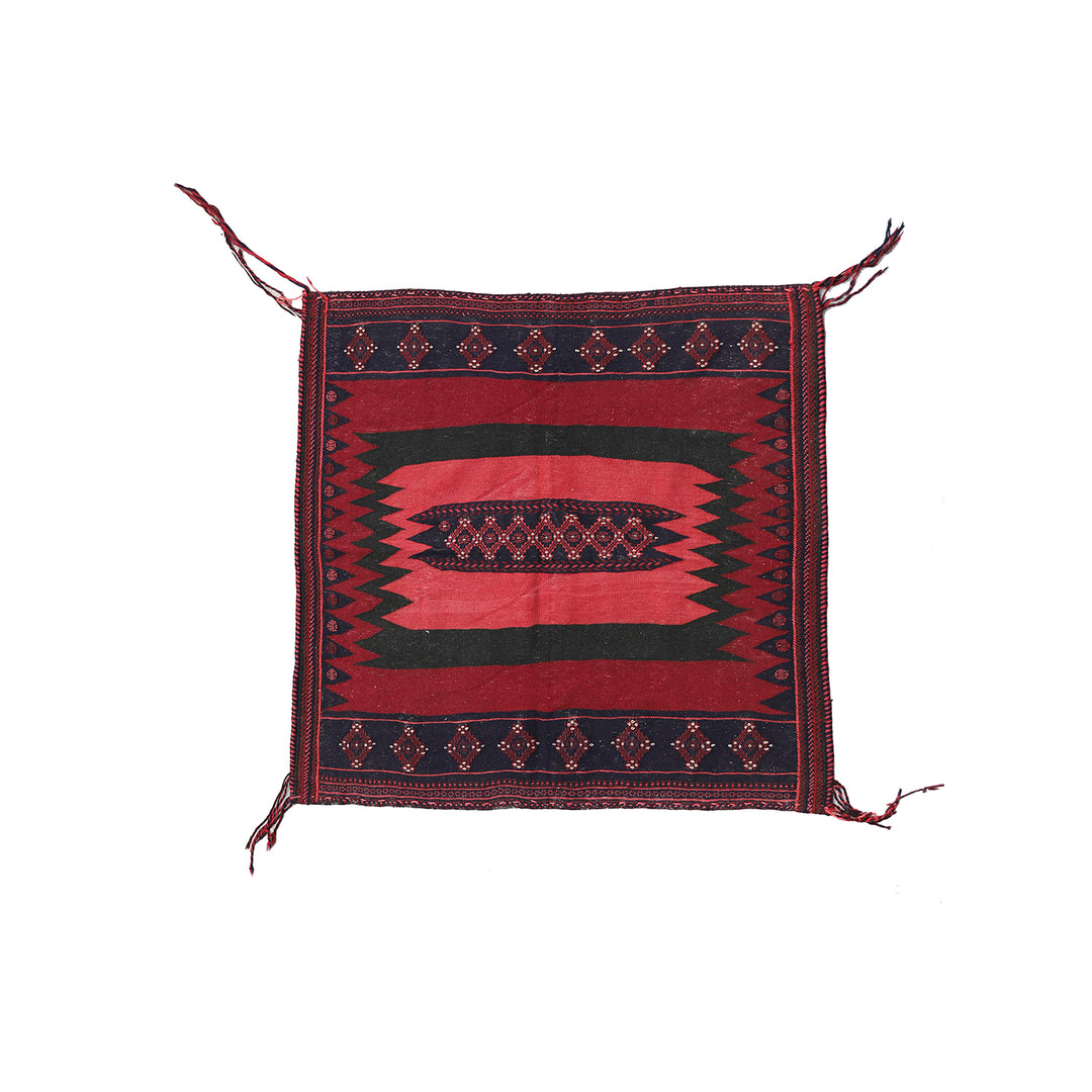 Decorative red and black patterned fabric with tassels on a white background