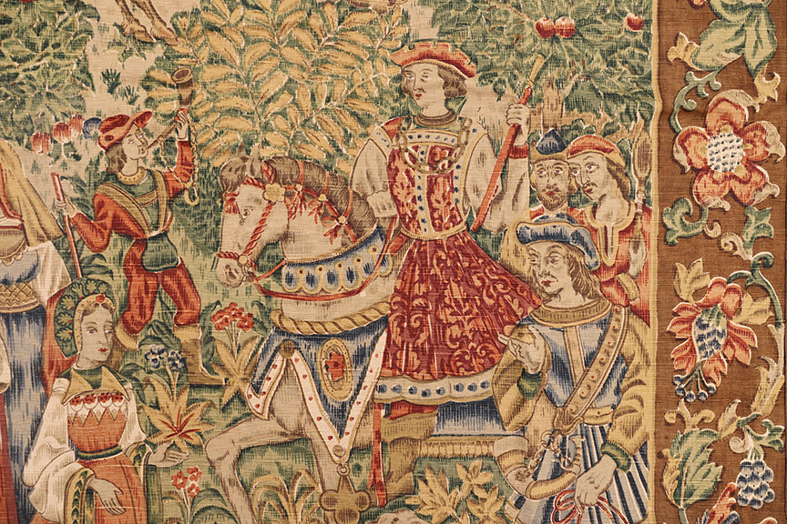 Decorative tapestry with a knight on horseback and other figures in a fantasy setting.