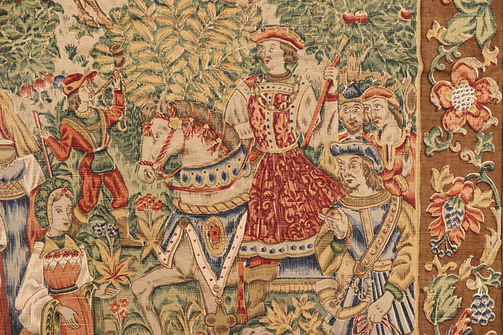 Decorative tapestry with a knight on horseback and other figures in a fantasy setting.