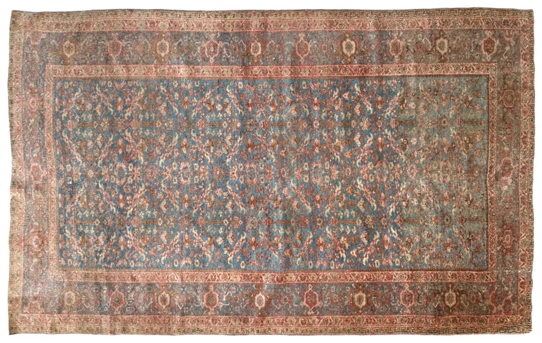 A rectangular vintage-style oriental rug with a dusty blue center field, surrounded by a warm rust-red border and intricate floral motifs in beige and muted orange tones.