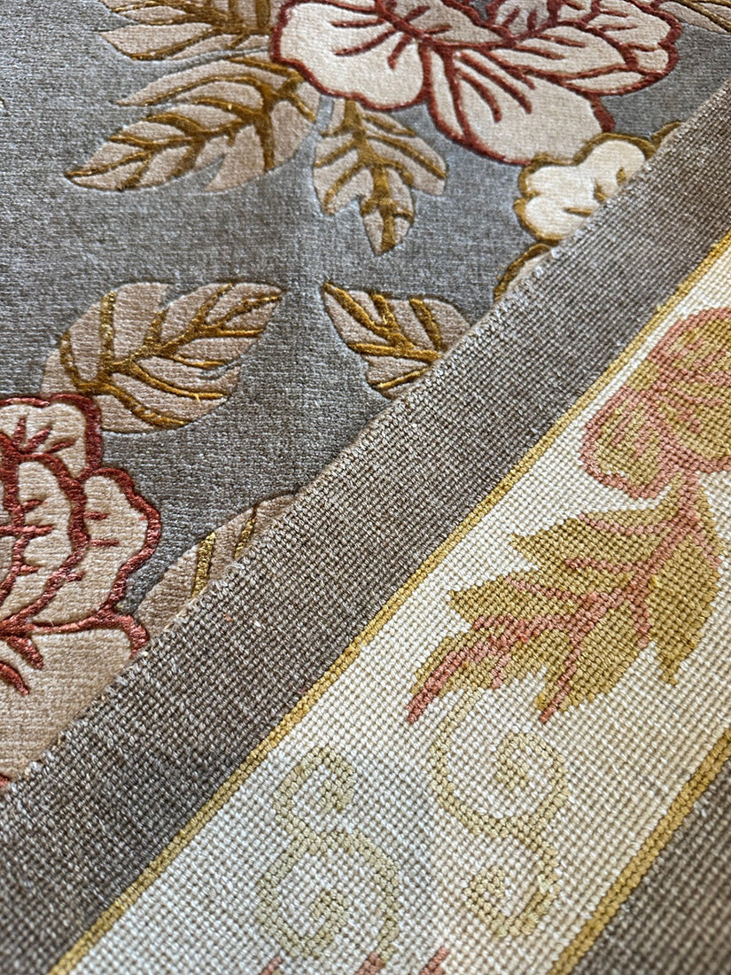 Close-up of a floral-patterned fabric with red, beige, and gold colors on a gray background.