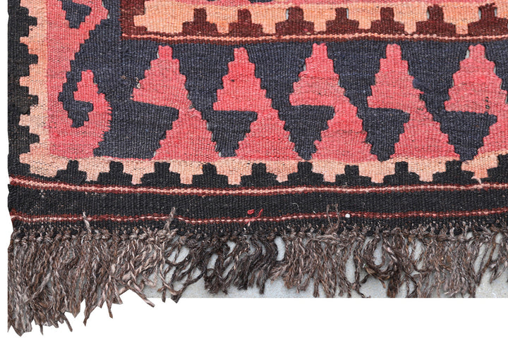 Close-up of a patterned fabric with pink and black triangles and fringes.
