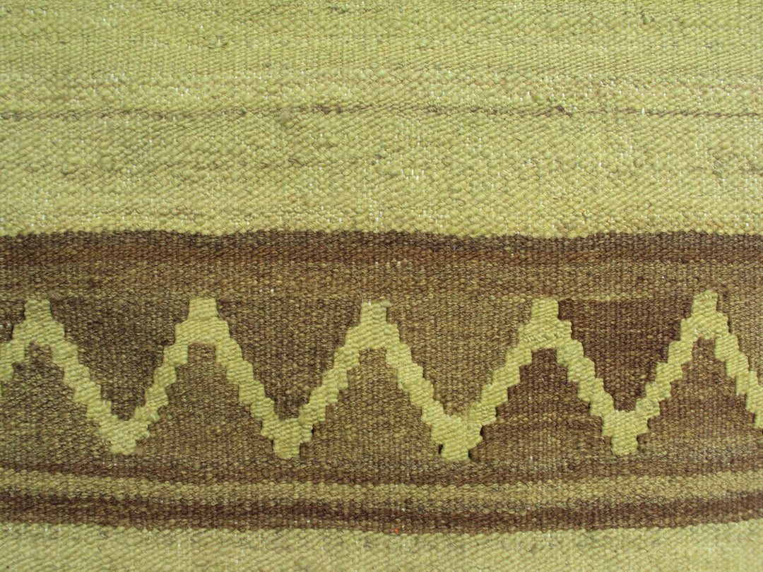 Handwoven green overdyed wool kilim with brown accents and geometric tribal design, crafted by Uzbek artisans in Afghanistan. Luxury flatweave from the Ariana Kilim Collection.