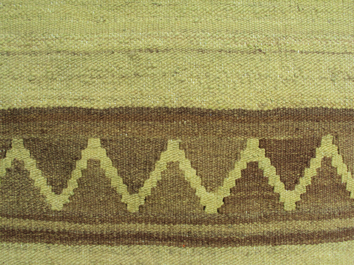 Handwoven green overdyed wool kilim with brown accents and geometric tribal design, crafted by Uzbek artisans in Afghanistan. Luxury flatweave from the Ariana Kilim Collection.