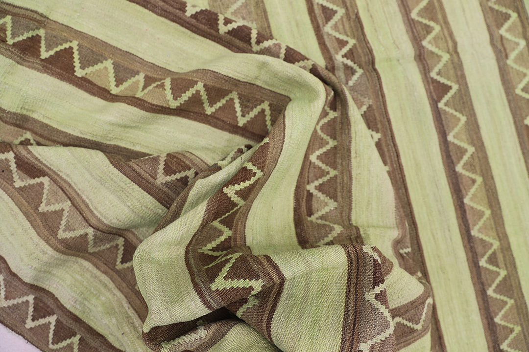 Handwoven green overdyed wool kilim with brown accents and geometric tribal design, crafted by Uzbek artisans in Afghanistan. Luxury flatweave from the Ariana Kilim Collection.