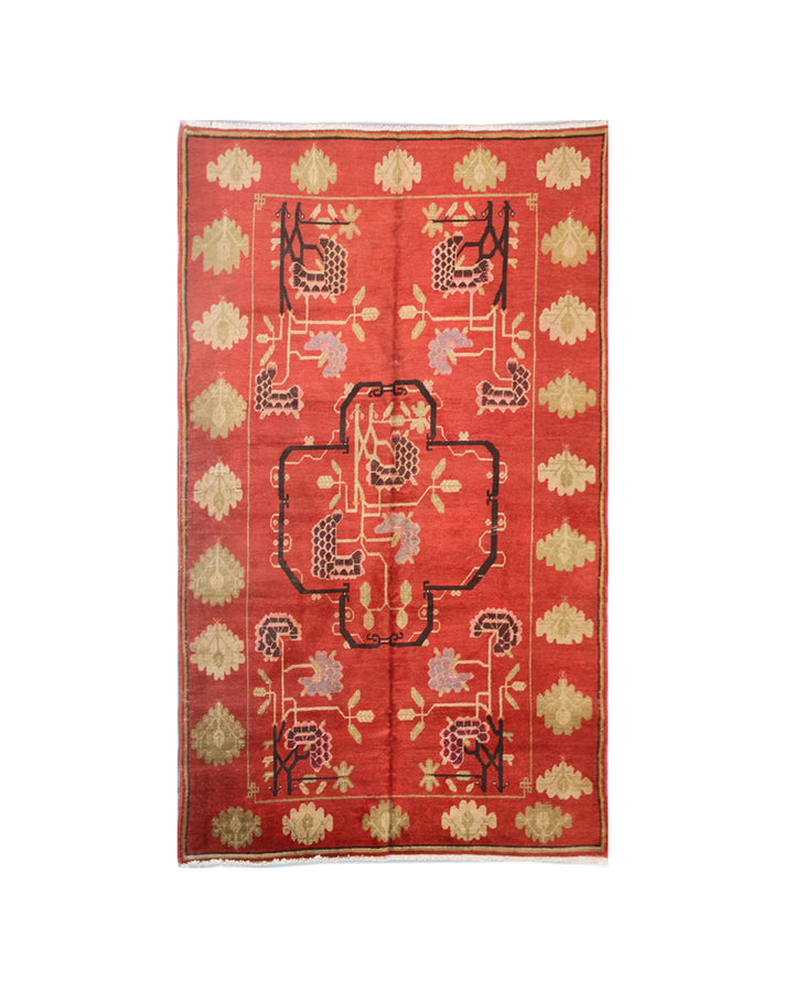 A rectangular red oriental rug with a central medallion and repeating floral motifs in beige, black, and muted pink, shown flat against a white background.
