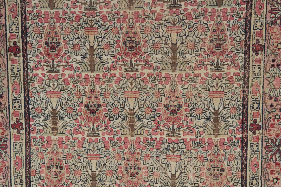 Antique Persian Kerman wool rug featuring an allover floral design with intricate palmettes and vine scrolls in soft pink, ivory, and deep navy blue