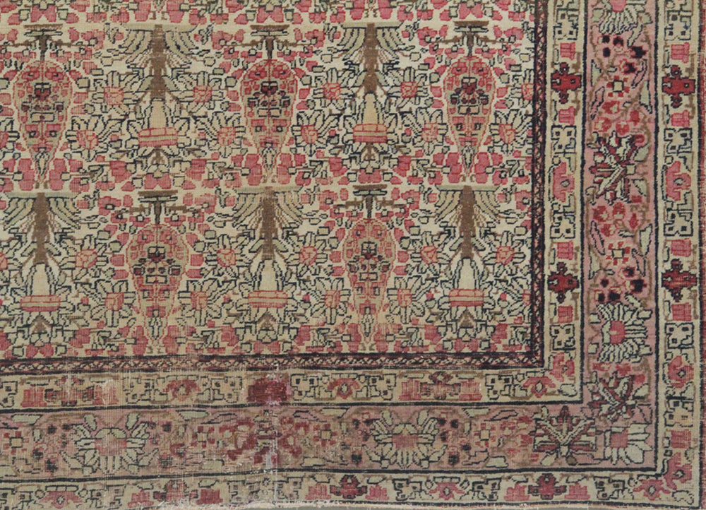 Antique Persian Kerman wool rug featuring an allover floral design with intricate palmettes and vine scrolls in soft pink, ivory, and deep navy blue