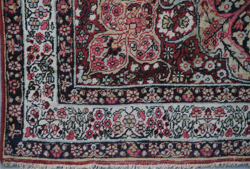 Antique Persian Kermanshah wool rug featuring a dark navy central medallion surrounded by floral motifs in ivory, pink, red, and tan