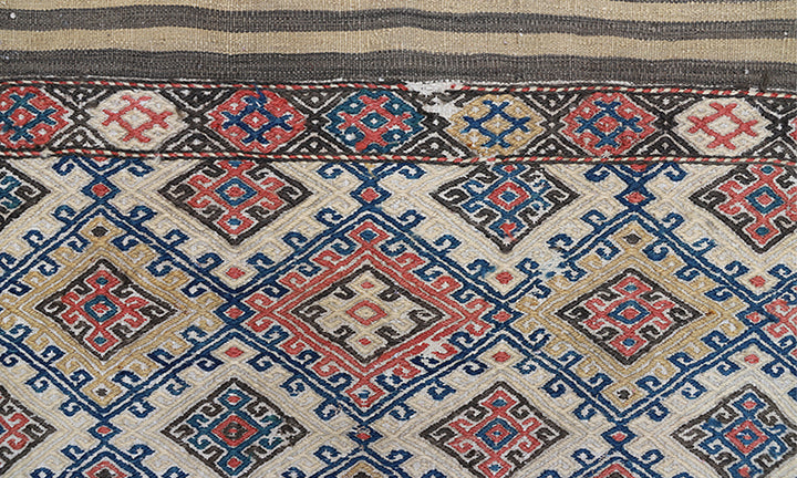 Close-up of a patterned fabric with geometric designs in red, blue, and beige.