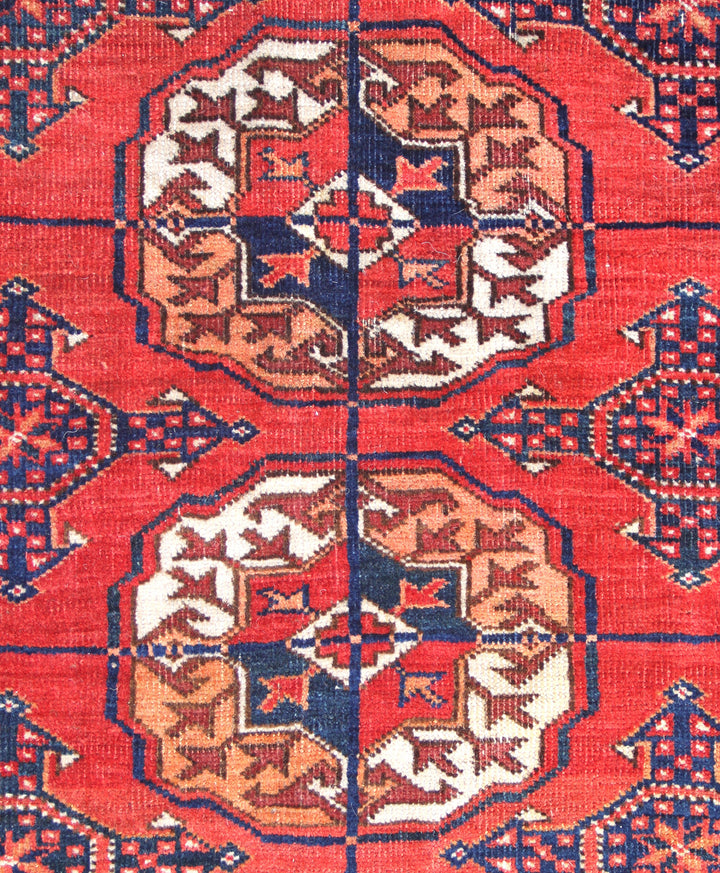 12'2" x 7'6" semi-antique Turkmen main carpet featuring a deep red field with hand-knotted geometric octagonal gul motifs and tribal borders.