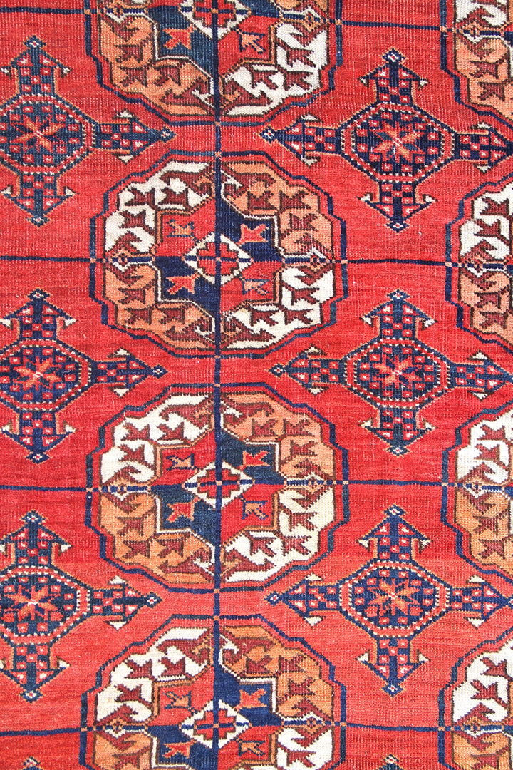 12'2" x 7'6" semi-antique Turkmen main carpet featuring a deep red field with hand-knotted geometric octagonal gul motifs and tribal borders.