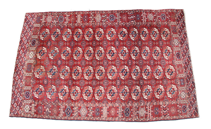 11'1" x 7'1" Antique Turkmen main rug featuring a deep red background with hand-knotted geometric motifs in navy, green, white, and brown.