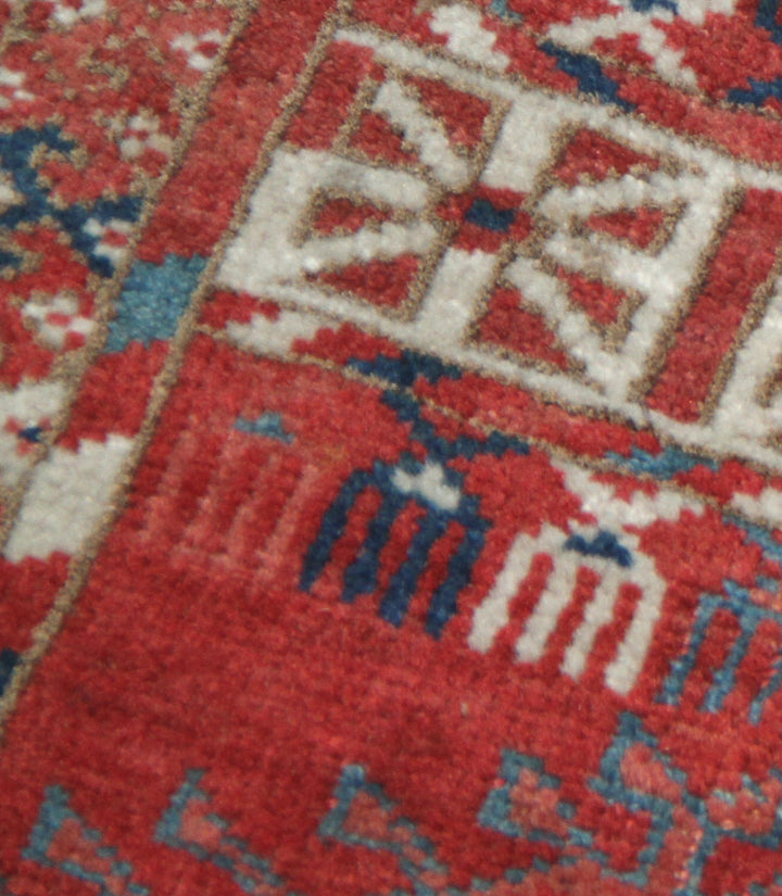 11'1" x 7'1" Antique Turkmen main rug featuring a deep red background with hand-knotted geometric motifs in navy, green, white, and brown.