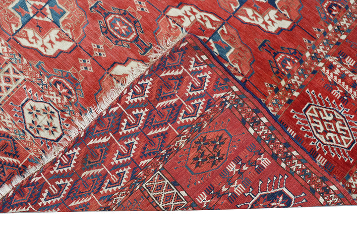 11'1" x 7'1" Antique Turkmen main rug featuring a deep red background with hand-knotted geometric motifs in navy, green, white, and brown.