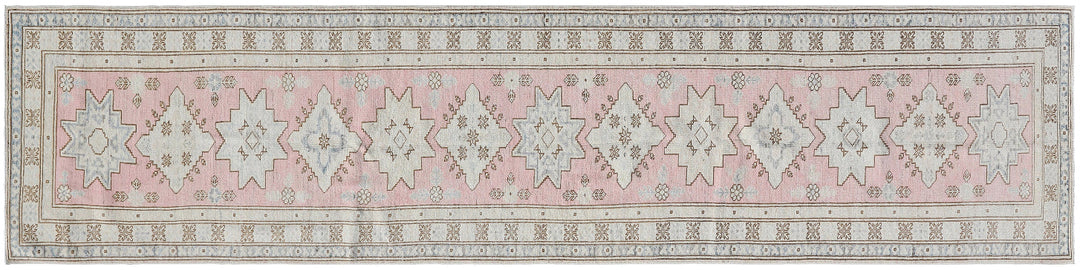 A long rectangular area rug with a traditional Persian-style pattern in dusty pink, beige, and gray, featuring repeating geometric star motifs.
