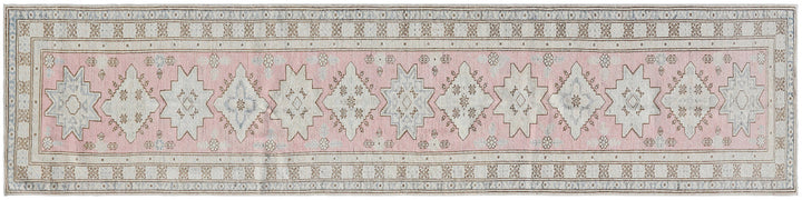A long rectangular area rug with a traditional Persian-style pattern in dusty pink, beige, and gray, featuring repeating geometric star motifs.