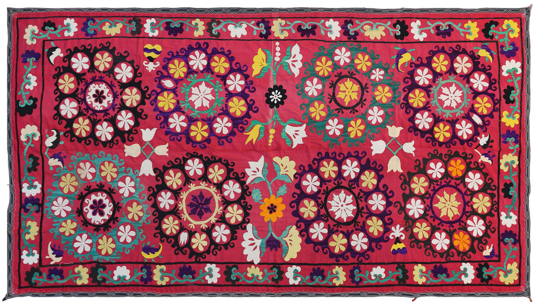 A vintage Uzbek Suzani textile featuring a multicolored floral pattern on a red background.