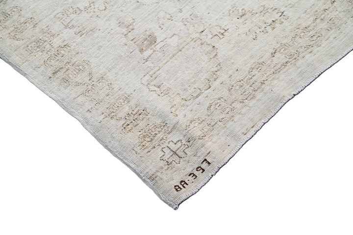 A close-up corner view of a distressed area rug with a faded beige and gray pattern on a white background.