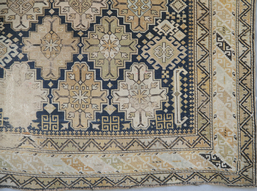 Distressed antique Caucasian Shirvan wool rug featuring geometric motifs in navy blue and tan with heavy distress and authentic age patina