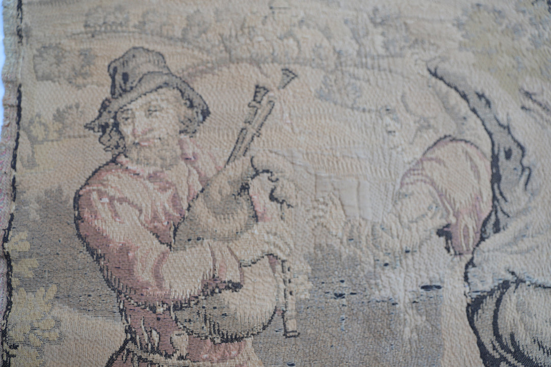 Early 20th-century French power-loomed tapestry depicting a man playing a pipe instrument and a man dancing in a pastoral setting, measuring 3 feet by 4 feet