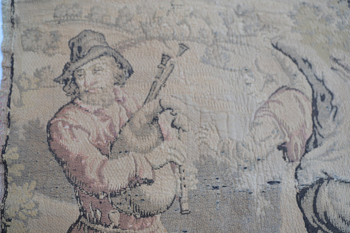 Early 20th-century French power-loomed tapestry depicting a man playing a pipe instrument and a man dancing in a pastoral setting, measuring 3 feet by 4 feet