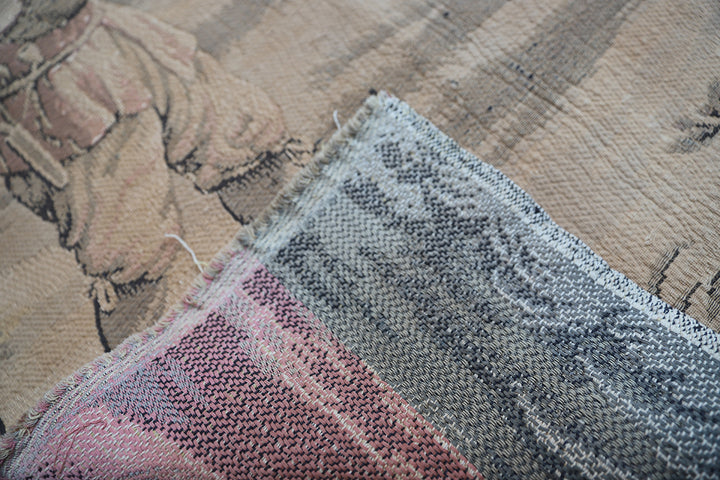 Early 20th-century French power-loomed tapestry depicting a man playing a pipe instrument and a man dancing in a pastoral setting, measuring 3 feet by 4 feet