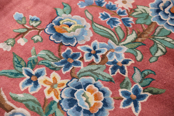 A 9x11 vintage Chinese Art Deco wool rug with a soft salmon pink background and sage green floral accents in the corners.