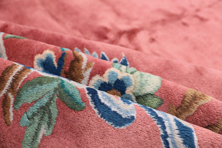 A 9x11 vintage Chinese Art Deco wool rug with a soft salmon pink background and sage green floral accents in the corners.