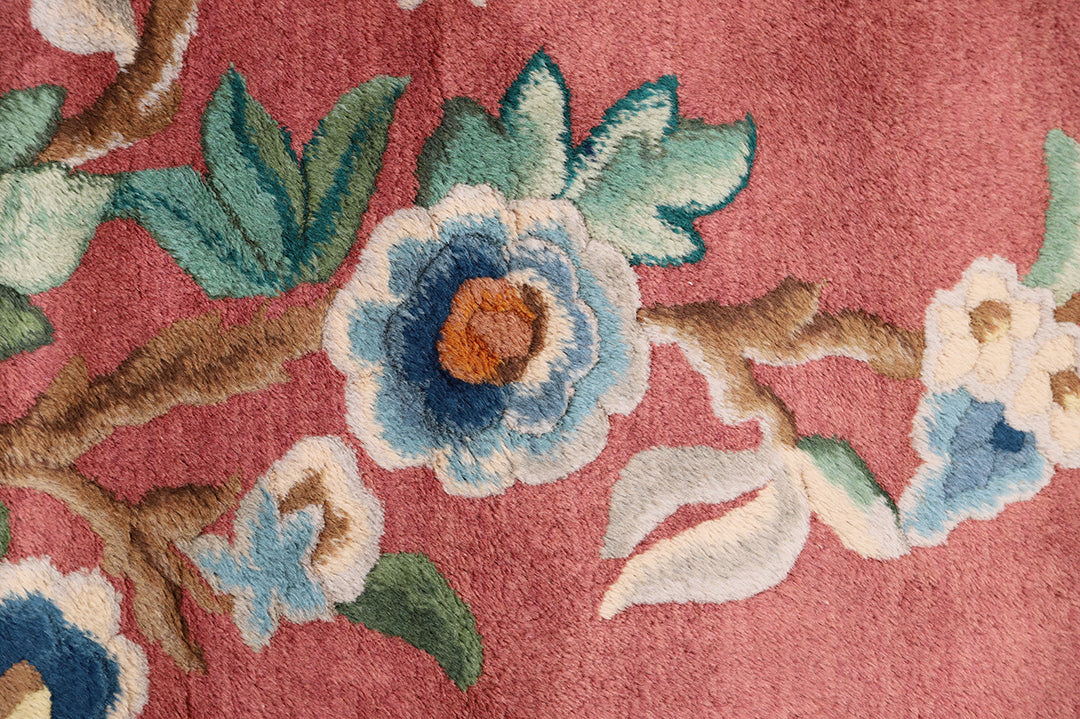 A 9x11 vintage Chinese Art Deco wool rug with a soft salmon pink background and sage green floral accents in the corners.