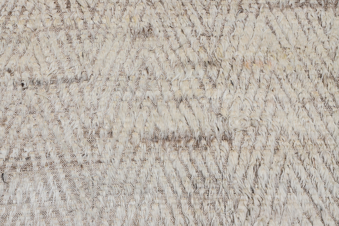 A close up of a cream ivory and brown high low pile chevron pattern contemporary modern moroccan wool area rug.