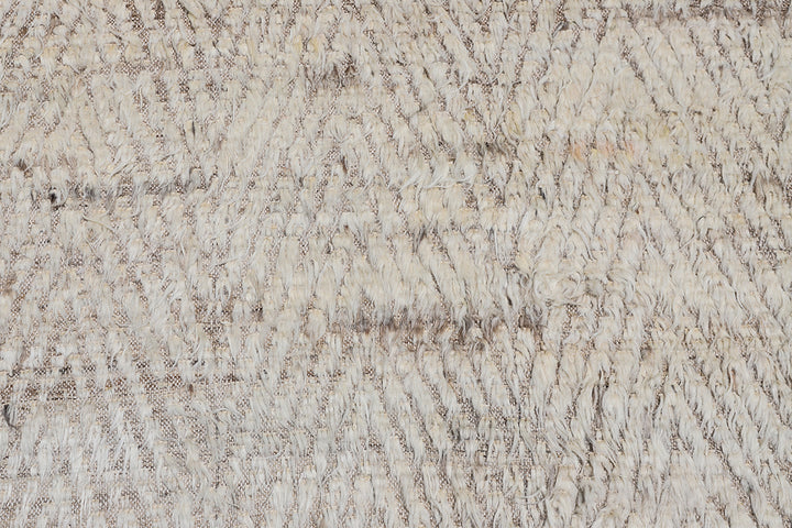 A close up of a cream ivory and brown high low pile chevron pattern contemporary modern moroccan wool area rug.