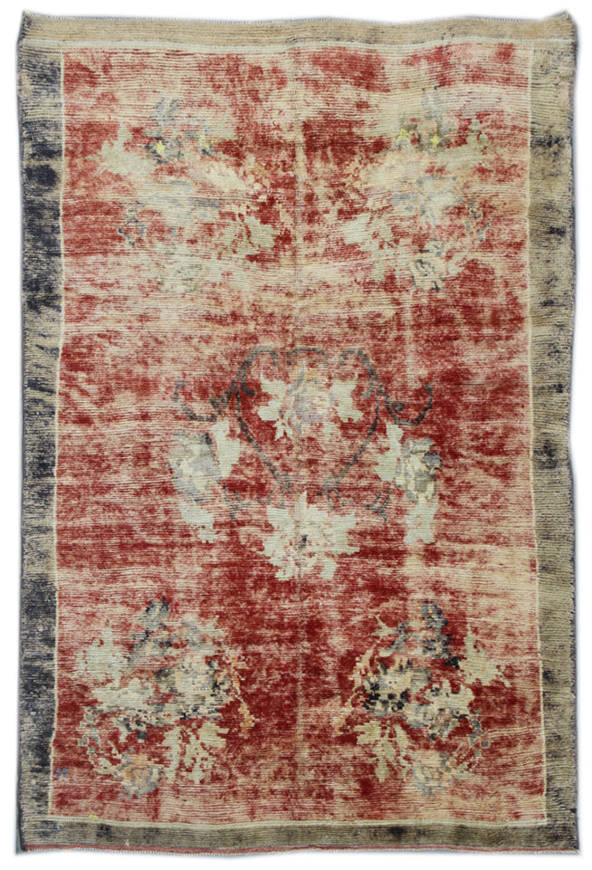 A vintage Turkish area rug with a red background and floral patterns in beige and dark red hues.