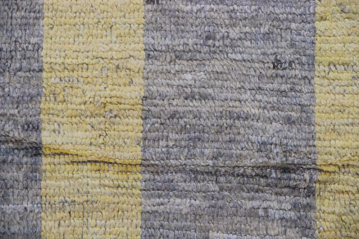 An overhead view of a massive 16x20 authentic Moroccan style long pile shag rug from the Ariana Barchi Collection, featuring a grey and yellow geometric pattern hand-woven by Hazara women weavers.