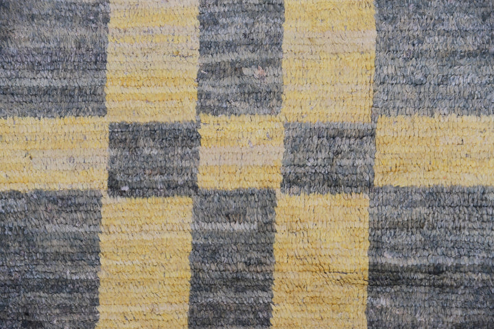An overhead view of a massive 16x20 authentic Moroccan style long pile shag rug from the Ariana Barchi Collection, featuring a grey and yellow geometric pattern hand-woven by Hazara women weavers.